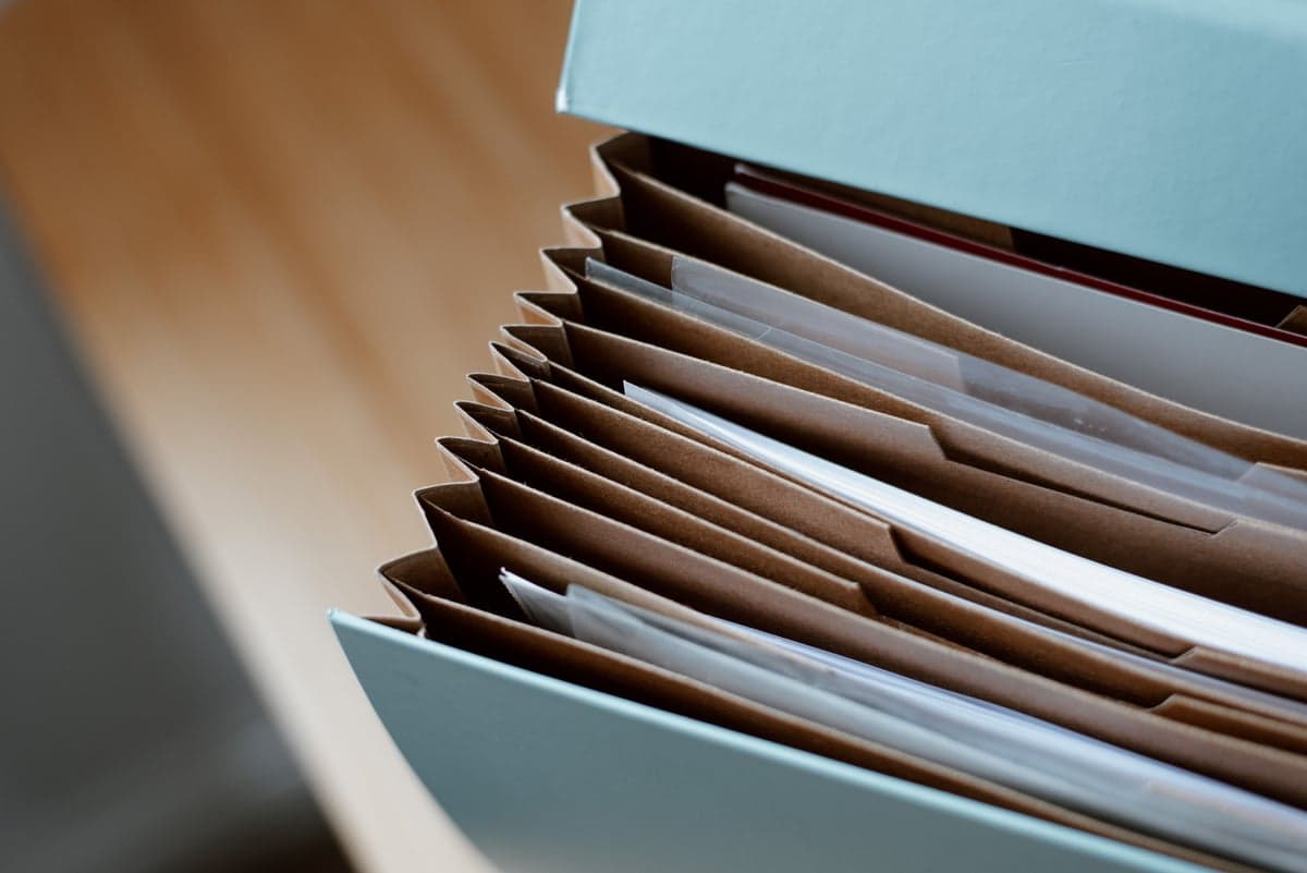 An open accordion file organizer with papers and envelopes tucked into its kraft-paper pockets