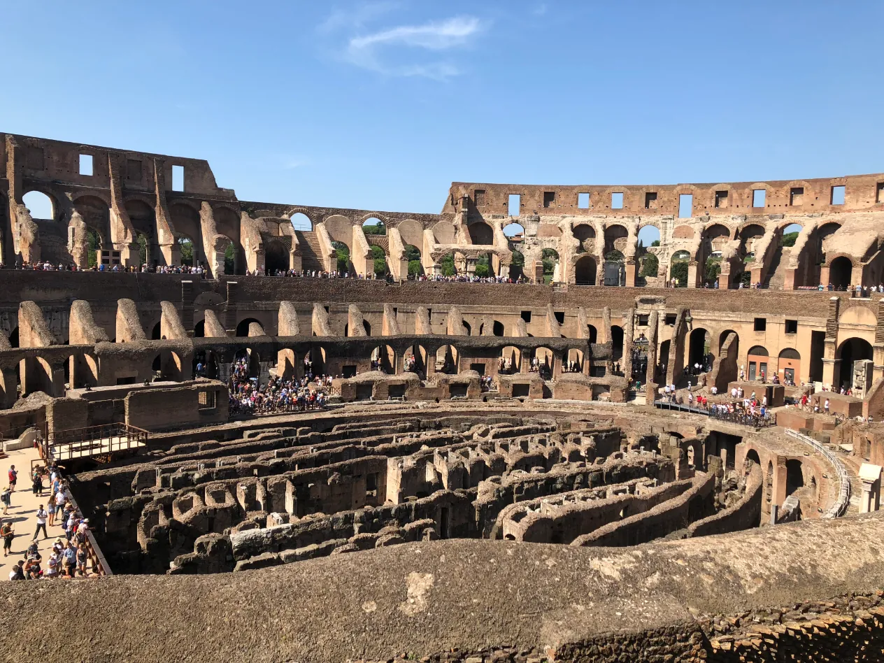The inside of the Colosseum in Rome on a sunny day, with tiers of arches above the exposed underground passages