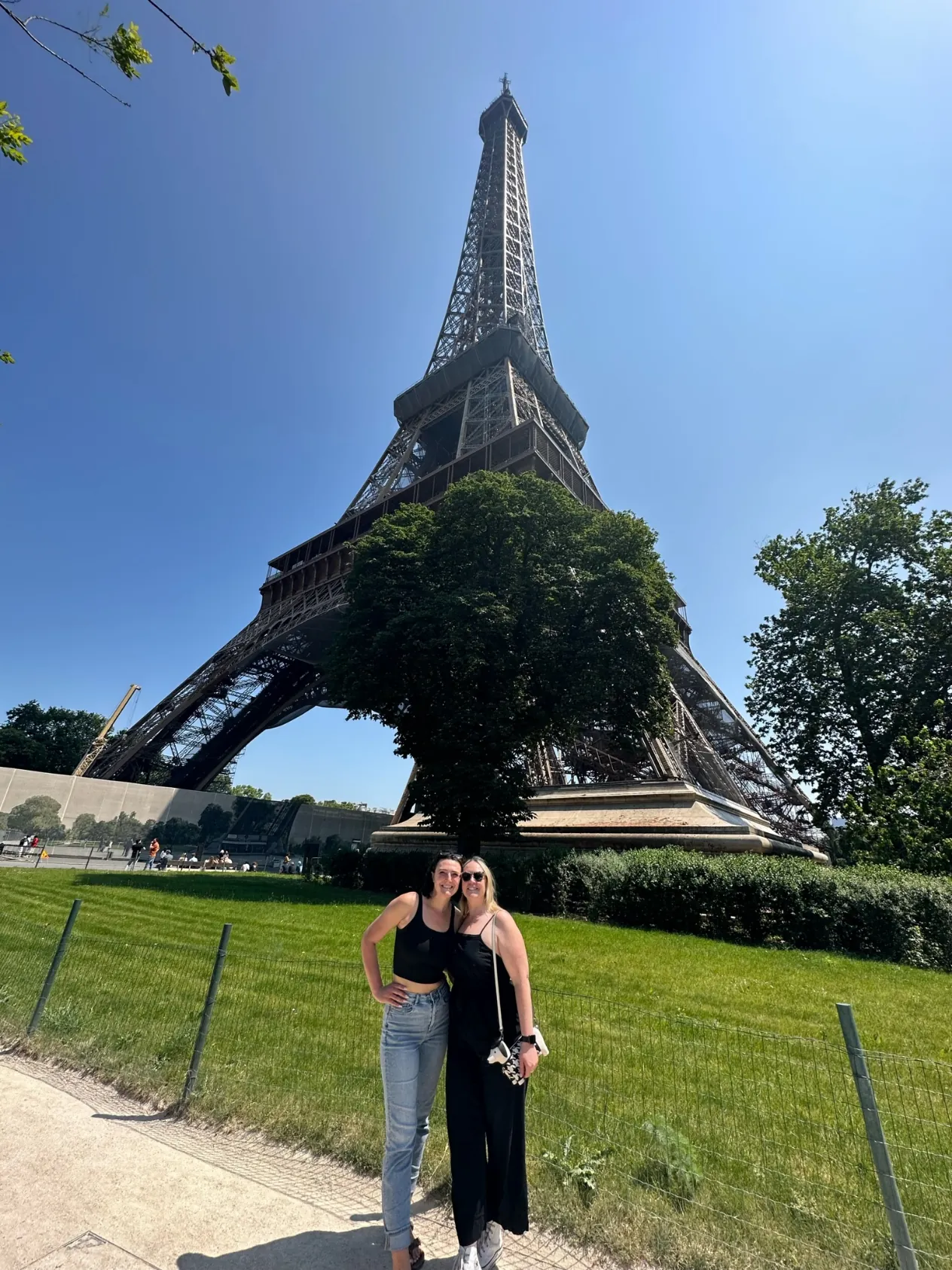 Two women standing on the grass below the Eiffel Tower on a clear day