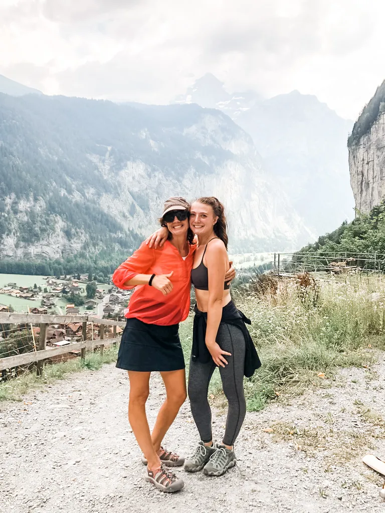 Two women smiling on a trail above the Lauterbrunnen valley, with cliffs and mountains behind them