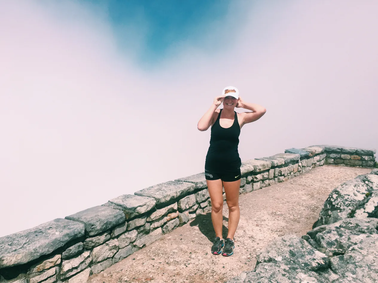 A woman in a cap standing on a stone path at the top of Table Mountain, with white cloud behind her