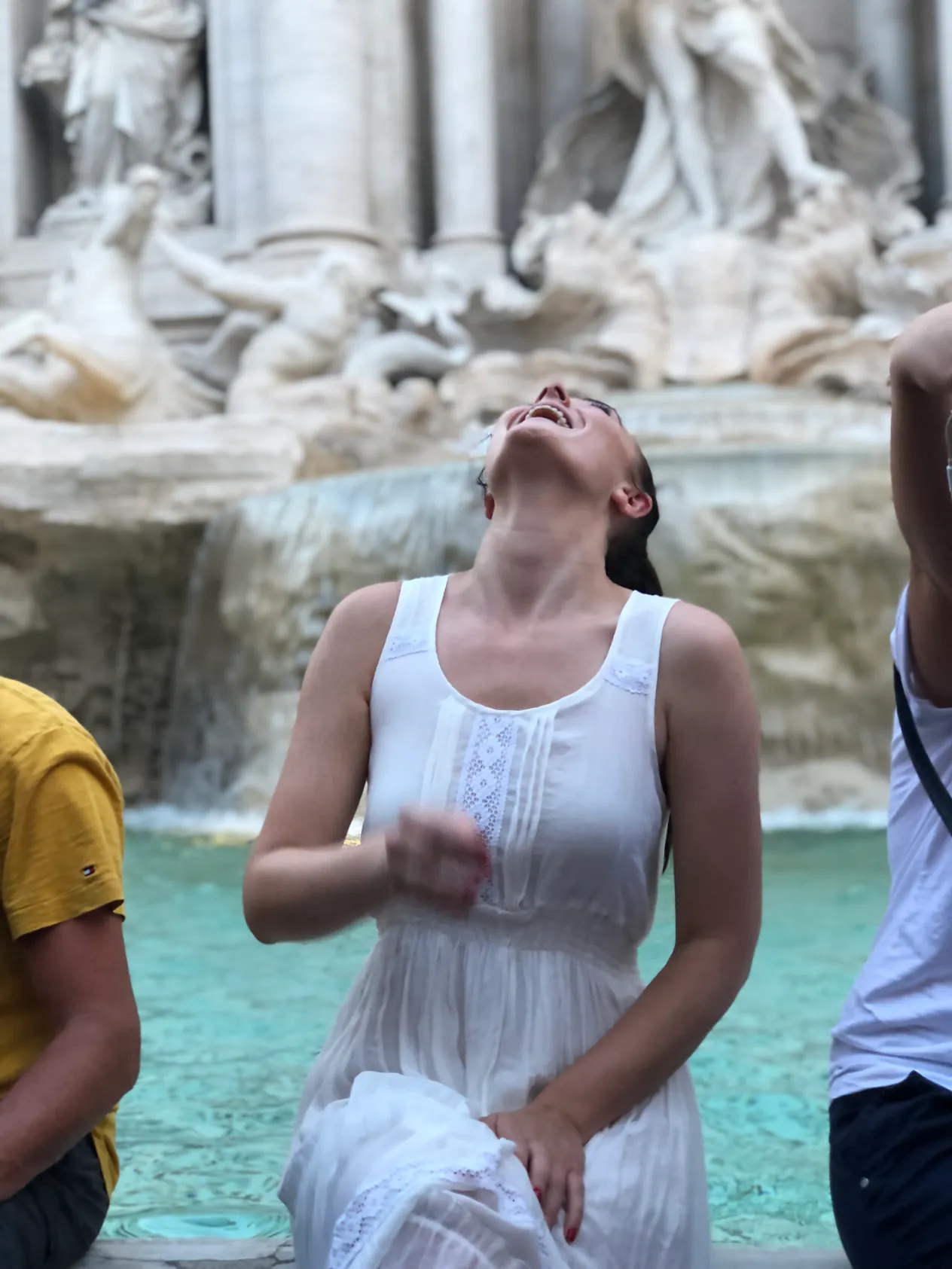 A woman in a white dress laughing in front of the Trevi Fountain