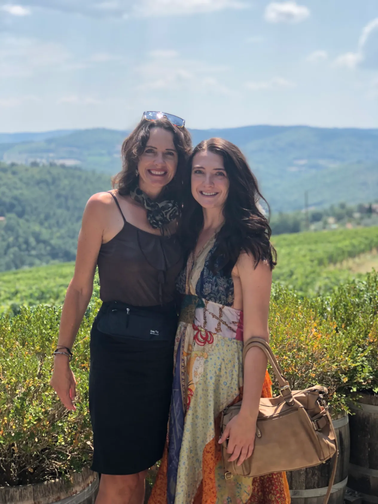 Two women standing in front of a vineyard and rolling green hills in Tuscany